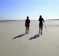 Zwei Frauen walken über den feuchten Sandstrand 