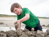 Junge in grünem TShirt baut eine Sandburg