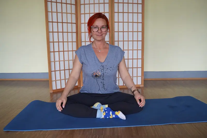 Brigitte Hube sitzt im Yogasitz auf einer Yogamatte.