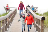 Kinder laufen fröhlich den Bohlenweg am Strand entlang während der Mutter-Kind-Kur